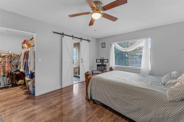 bedroom with a spacious closet, a barn door, dark wood-type flooring, a textured ceiling, and a closet