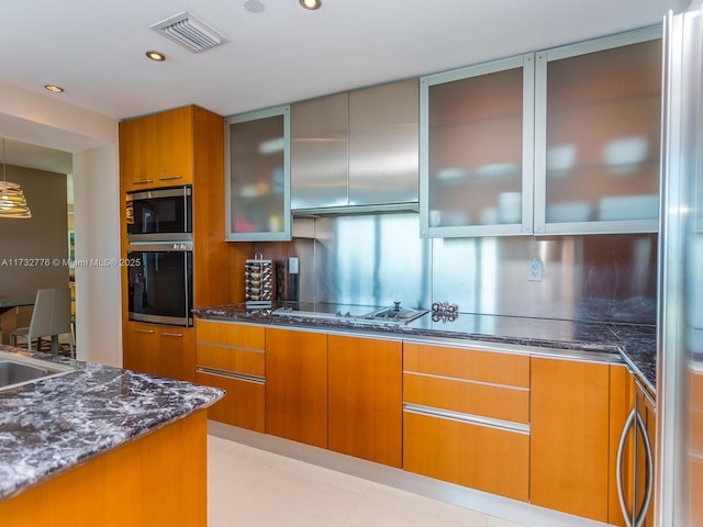 kitchen with stainless steel microwave, black electric stovetop, sink, and dark stone countertops