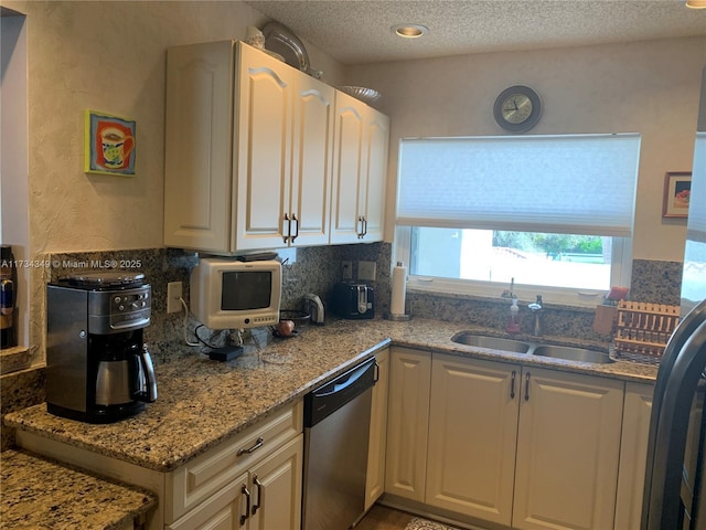 kitchen with sink, white cabinetry, light stone counters, a textured ceiling, and stainless steel dishwasher