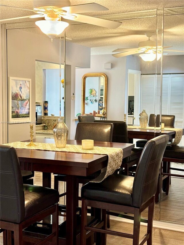 dining space featuring wood-type flooring, ceiling fan, and a textured ceiling