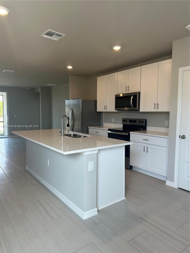 kitchen with appliances with stainless steel finishes, a center island with sink, and white cabinets