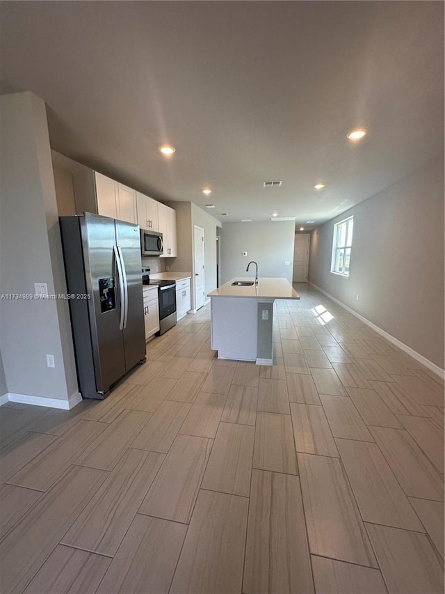 kitchen featuring white cabinetry, sink, stainless steel appliances, and an island with sink