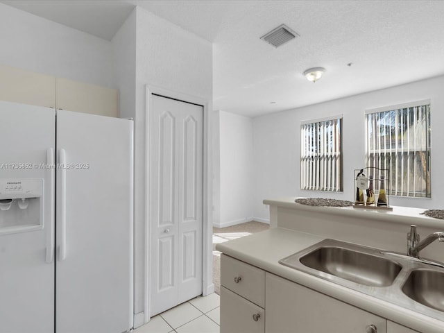 kitchen with sink, white refrigerator with ice dispenser, white cabinets, a textured ceiling, and light tile patterned flooring