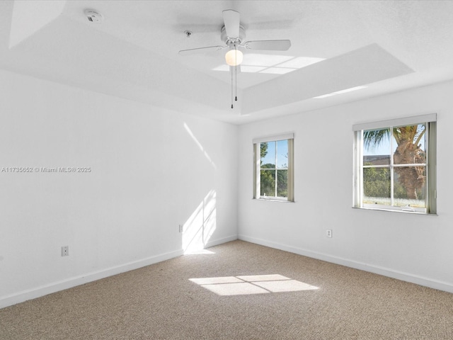 carpeted empty room with ceiling fan, plenty of natural light, and a tray ceiling