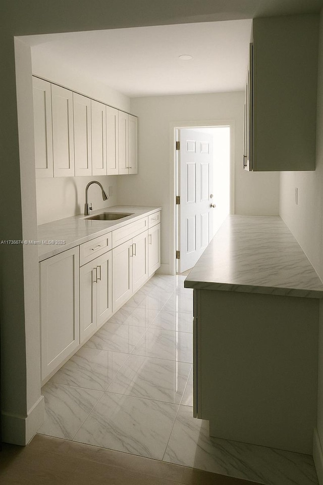 kitchen featuring white cabinets, light countertops, marble finish floor, and a sink
