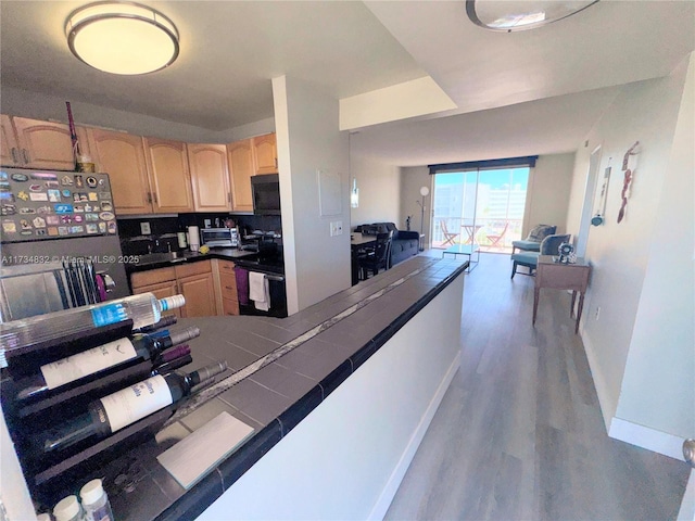 kitchen featuring tile countertops, stainless steel refrigerator, wood-type flooring, and light brown cabinets