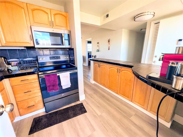 kitchen with decorative backsplash, stainless steel appliances, tile counters, and light hardwood / wood-style flooring