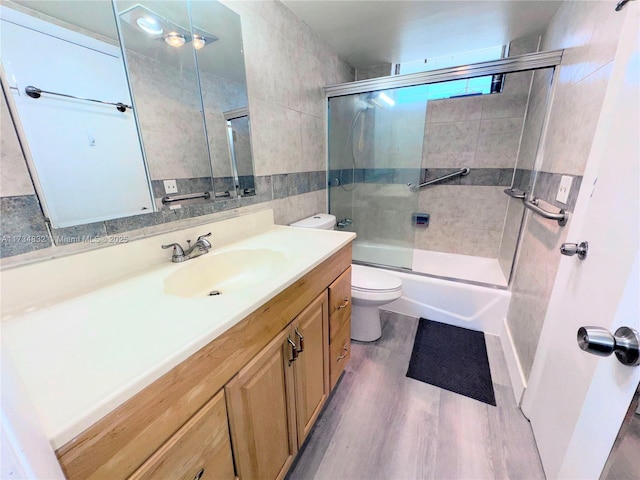 full bathroom with hardwood / wood-style flooring, tile walls, bath / shower combo with glass door, vanity, and toilet