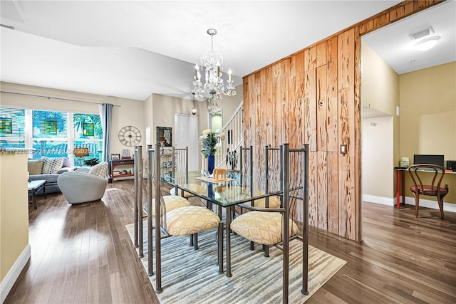 dining room featuring wood walls, dark hardwood / wood-style floors, and a notable chandelier