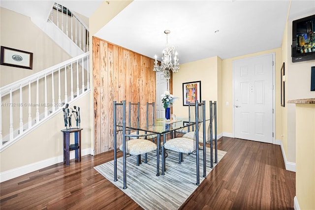 dining room featuring dark wood-type flooring, wooden walls, and a chandelier