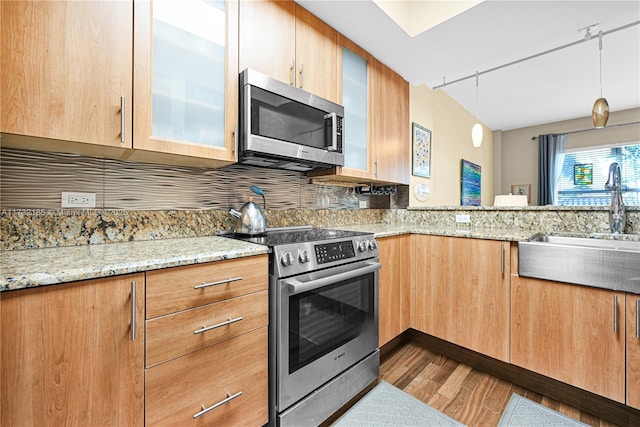 kitchen featuring pendant lighting, wood-type flooring, sink, stainless steel appliances, and light stone countertops