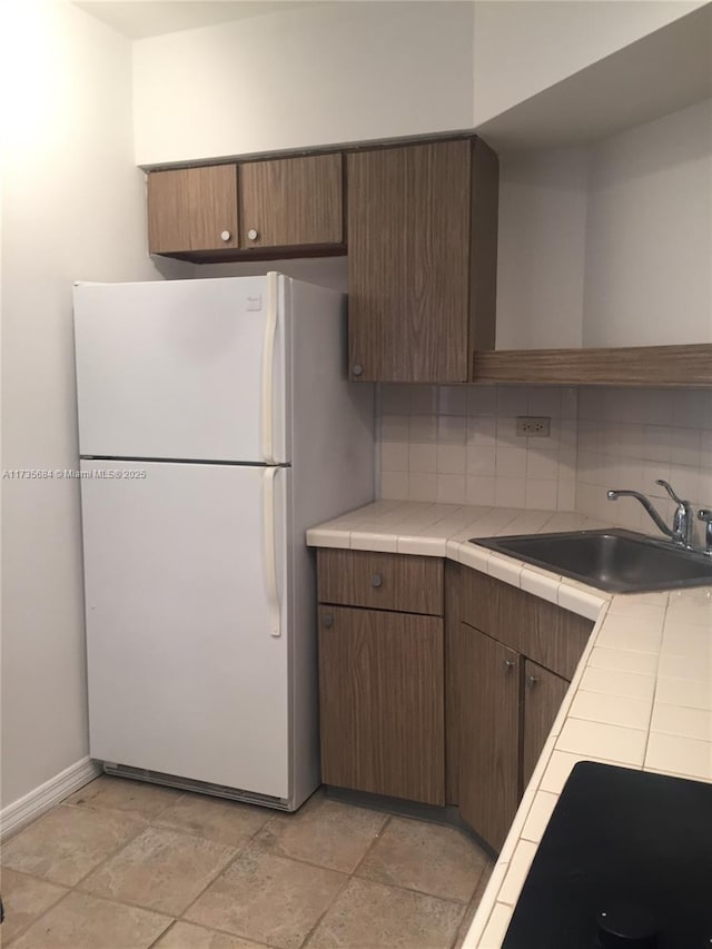 kitchen featuring sink, backsplash, tile countertops, and white fridge