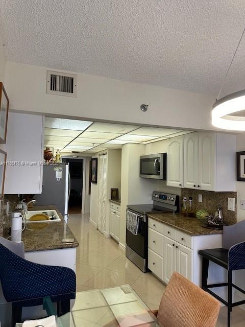 kitchen with tasteful backsplash, stainless steel appliances, light tile patterned floors, and white cabinets