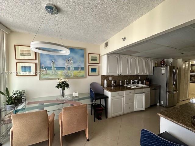 kitchen with visible vents, light tile patterned flooring, freestanding refrigerator, a sink, and dark countertops