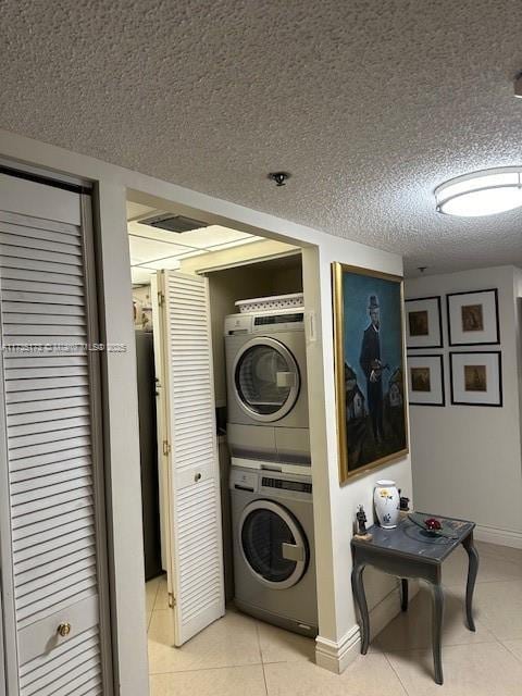 laundry room with a textured ceiling, stacked washing maching and dryer, light tile patterned flooring, baseboards, and laundry area