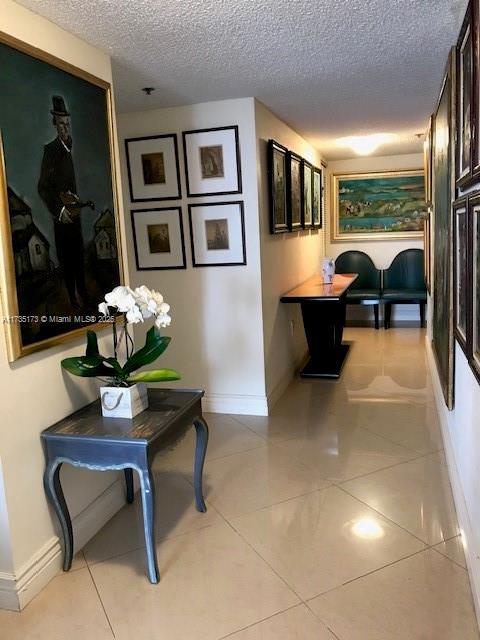 hallway with light tile patterned flooring, a textured ceiling, and baseboards