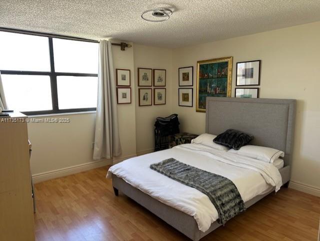 bedroom featuring wood finished floors, baseboards, and a textured ceiling