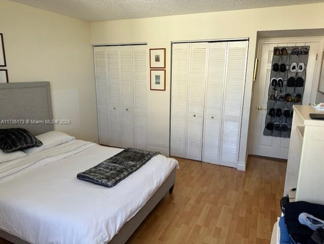 bedroom featuring light wood finished floors, two closets, and a textured ceiling