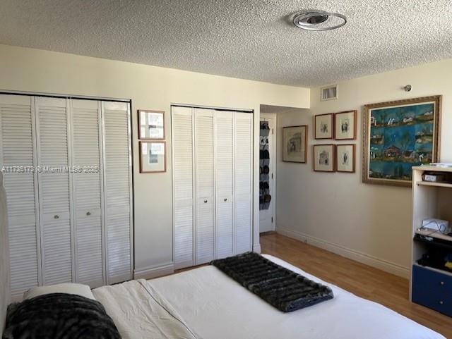 bedroom with visible vents, multiple closets, a textured ceiling, and wood finished floors