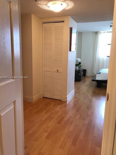 hall featuring light wood-style flooring, a textured ceiling, and baseboards