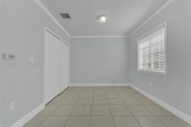 unfurnished bedroom featuring crown molding, light tile patterned flooring, and a closet