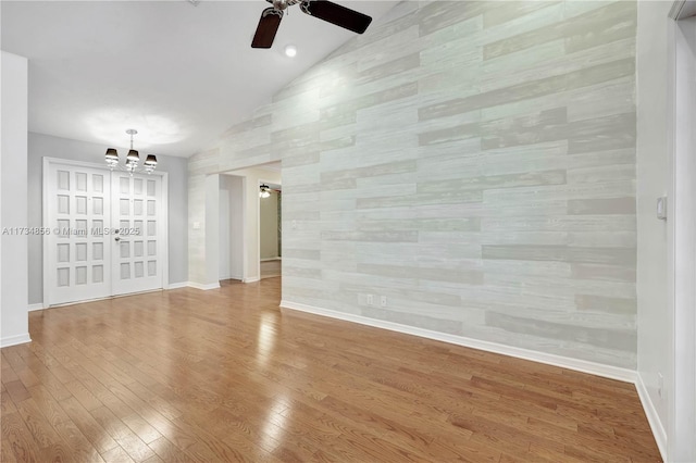 unfurnished living room with ceiling fan with notable chandelier, vaulted ceiling, and wood-type flooring