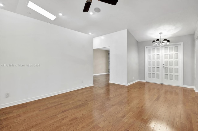 empty room with ceiling fan with notable chandelier and light wood-type flooring