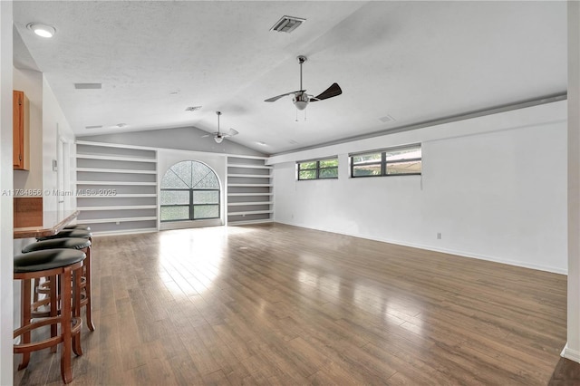 unfurnished living room featuring vaulted ceiling, hardwood / wood-style flooring, ceiling fan, a textured ceiling, and built in shelves