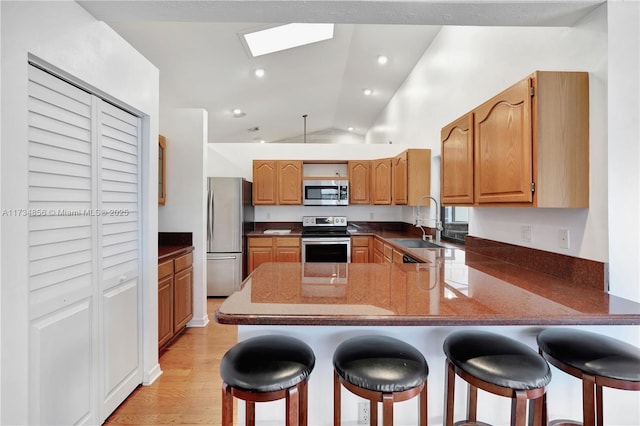 kitchen with vaulted ceiling with skylight, sink, a breakfast bar area, kitchen peninsula, and stainless steel appliances