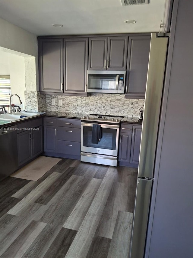 kitchen with dark wood-type flooring, sink, gray cabinetry, appliances with stainless steel finishes, and decorative backsplash