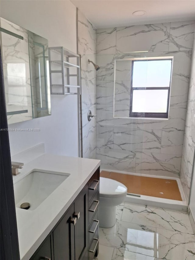 bathroom with a tile shower, vanity, and toilet