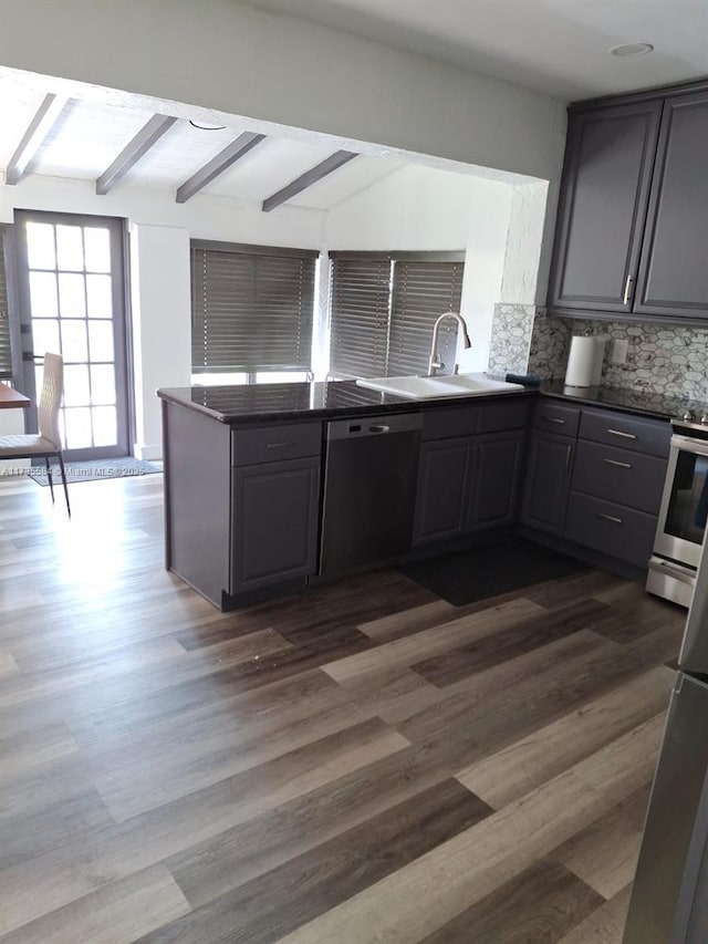 kitchen with appliances with stainless steel finishes, sink, decorative backsplash, kitchen peninsula, and dark wood-type flooring