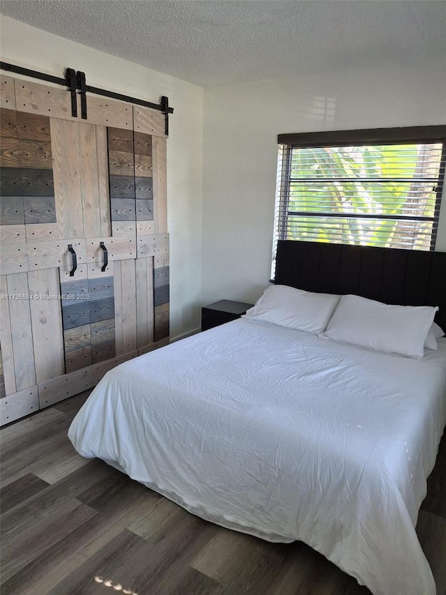 bedroom with wood-type flooring, a barn door, and a textured ceiling