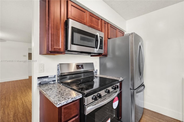 kitchen with appliances with stainless steel finishes, light stone countertops, a textured ceiling, and hardwood / wood-style flooring