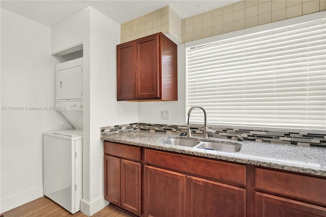 kitchen with light stone countertops, stacked washer and clothes dryer, backsplash, sink, and light wood-type flooring