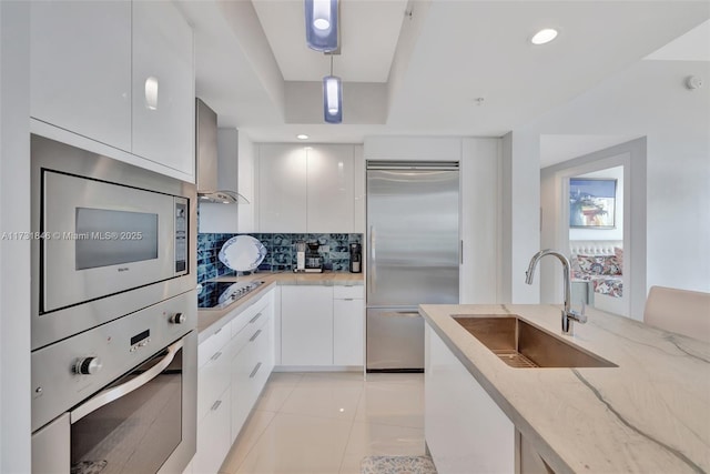 kitchen featuring white cabinetry, built in appliances, decorative light fixtures, and sink