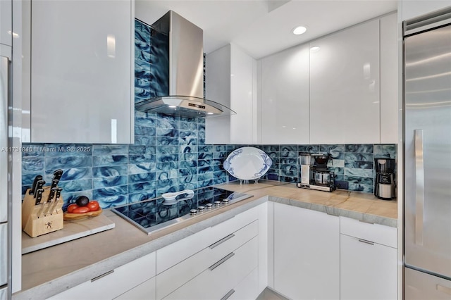 kitchen with wall chimney range hood, stovetop, white cabinets, and built in refrigerator