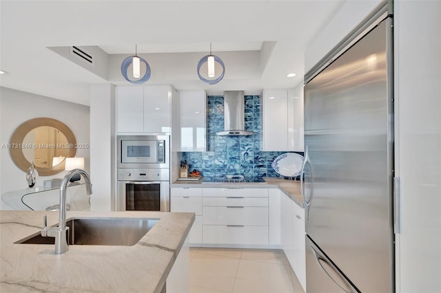 kitchen with appliances with stainless steel finishes, pendant lighting, white cabinetry, sink, and wall chimney range hood