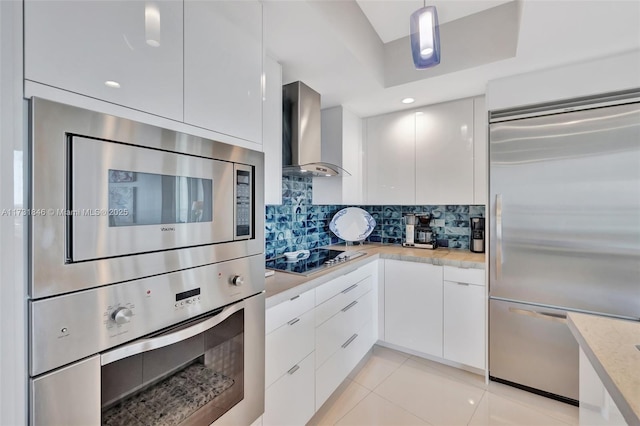 kitchen with white cabinetry, built in appliances, hanging light fixtures, decorative backsplash, and wall chimney range hood