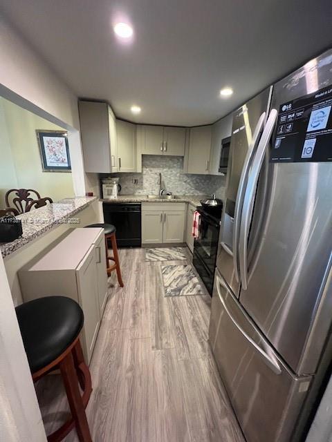 kitchen featuring a breakfast bar area, black appliances, decorative backsplash, kitchen peninsula, and light wood-type flooring