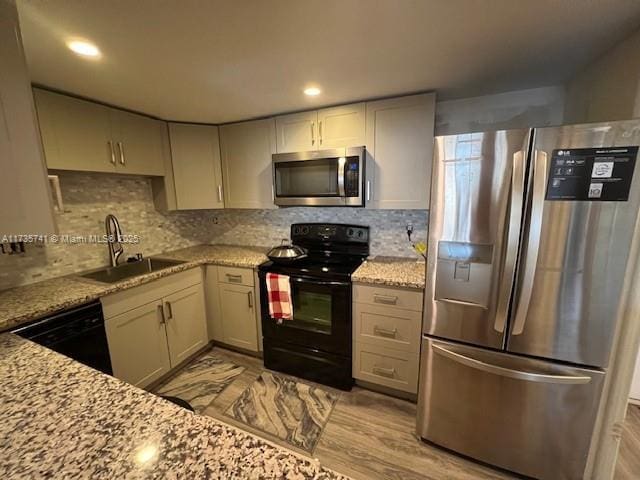 kitchen featuring light stone counters, backsplash, sink, and black appliances