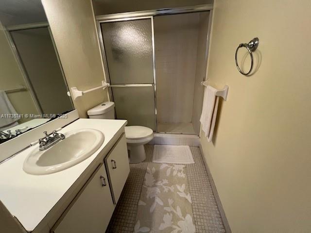 bathroom featuring a shower with door, vanity, tile patterned floors, and toilet