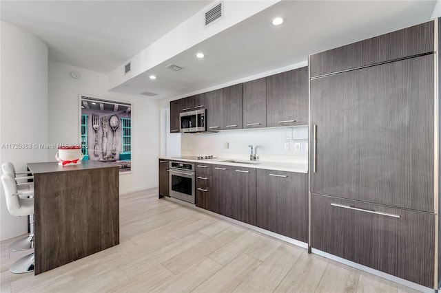 kitchen featuring sink, a kitchen bar, light hardwood / wood-style floors, stainless steel appliances, and dark brown cabinets