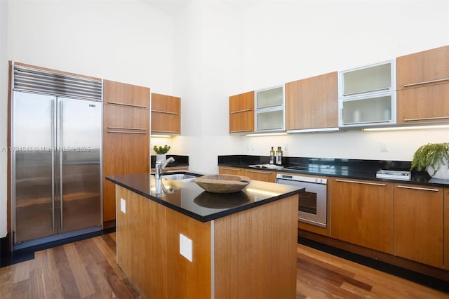 kitchen with an island with sink, sink, a high ceiling, stainless steel built in fridge, and wall oven