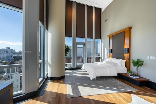 bedroom with a wall of windows, wood-type flooring, and a high ceiling