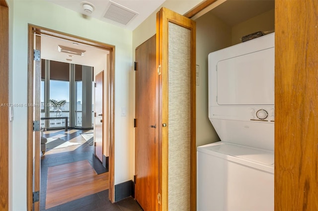 laundry room with stacked washer / drying machine and dark wood-type flooring