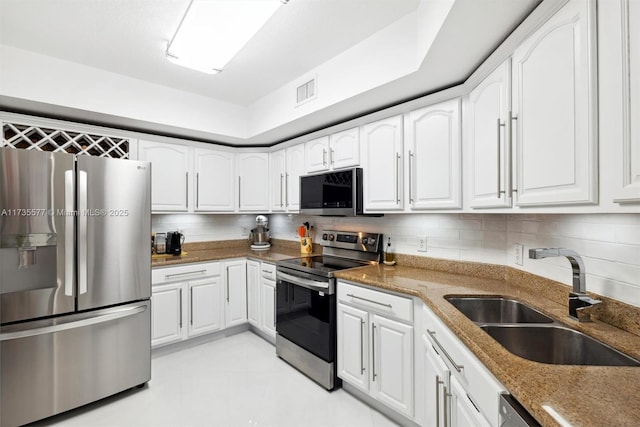 kitchen with sink, appliances with stainless steel finishes, white cabinetry, backsplash, and dark stone counters