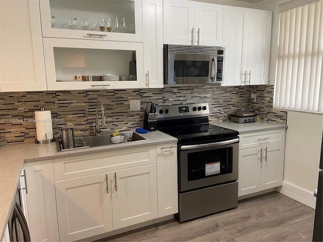 kitchen featuring sink, light hardwood / wood-style flooring, stainless steel appliances, white cabinets, and decorative backsplash