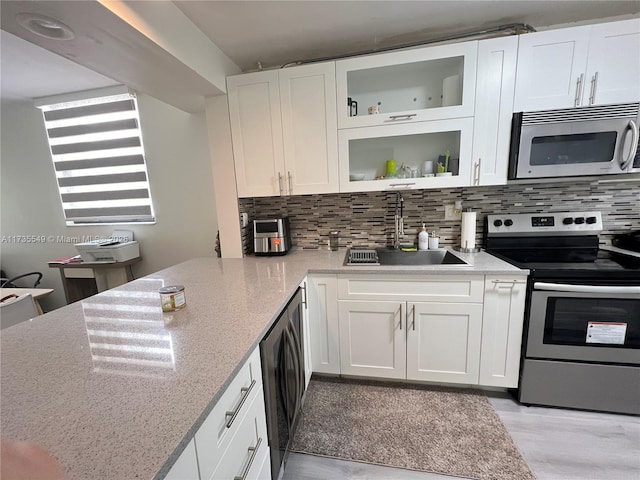kitchen with sink, kitchen peninsula, stainless steel appliances, decorative backsplash, and white cabinets