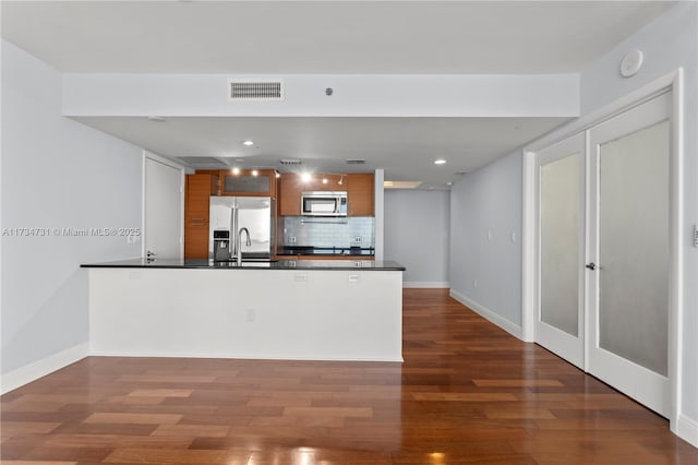 kitchen with dark hardwood / wood-style flooring, backsplash, kitchen peninsula, and appliances with stainless steel finishes